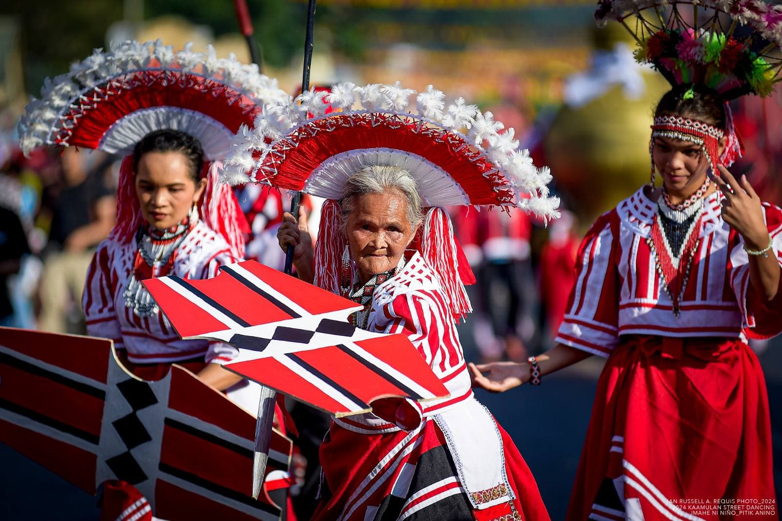 An elder and two other performers in coordinated red, white, and black dress during a Kaamulan street presentation in Malaybalay City
